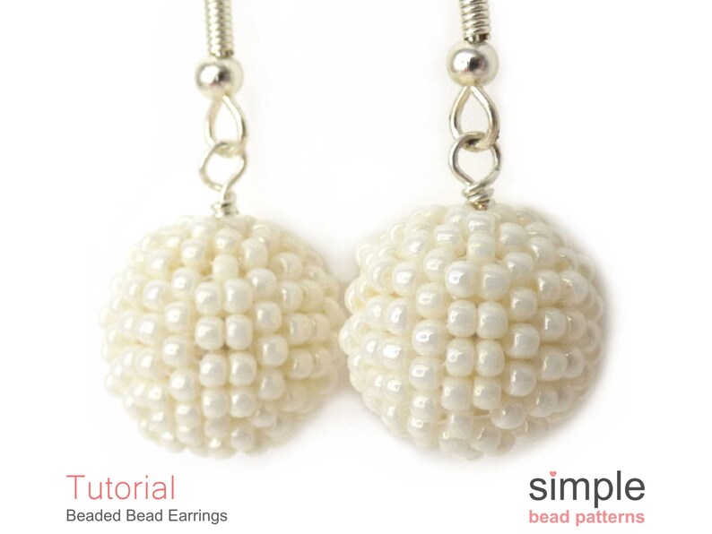 May include: A pair of white beaded earrings with silver hooks. The beads are small and round, creating a spherical shape. The earrings are simple and elegant.