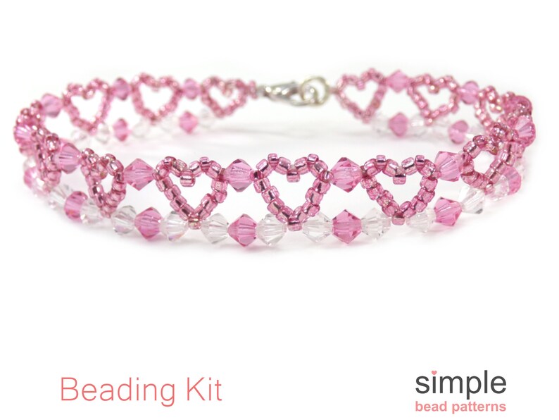 Op de afbeelding: Een armband van roze en heldere kristallen kralen met een hartvormig ontwerp. De armband is gemaakt van rocailles en heeft een zilveren sluiting. Kralenset.