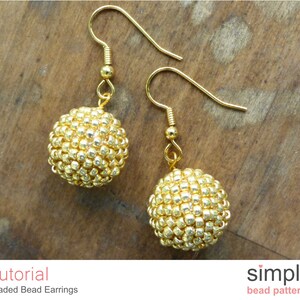 May include: Gold beaded earrings with a simple design. The earrings are made with small, round beads that are strung together to create a sphere shape. The earrings are attached to gold hooks.