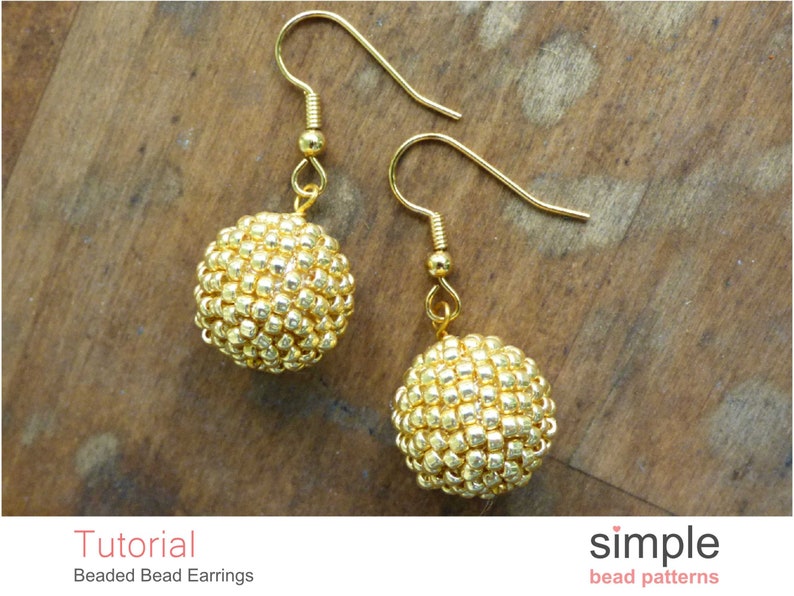 May include: Gold beaded earrings with a simple design. The earrings are made with small, round beads that are strung together to create a sphere shape. The earrings are attached to gold hooks.