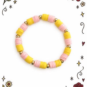 Armband van kleikralen in bananensplit-vorm, roze, geel en goudkleurige kralen, met een buigbaar koord.
