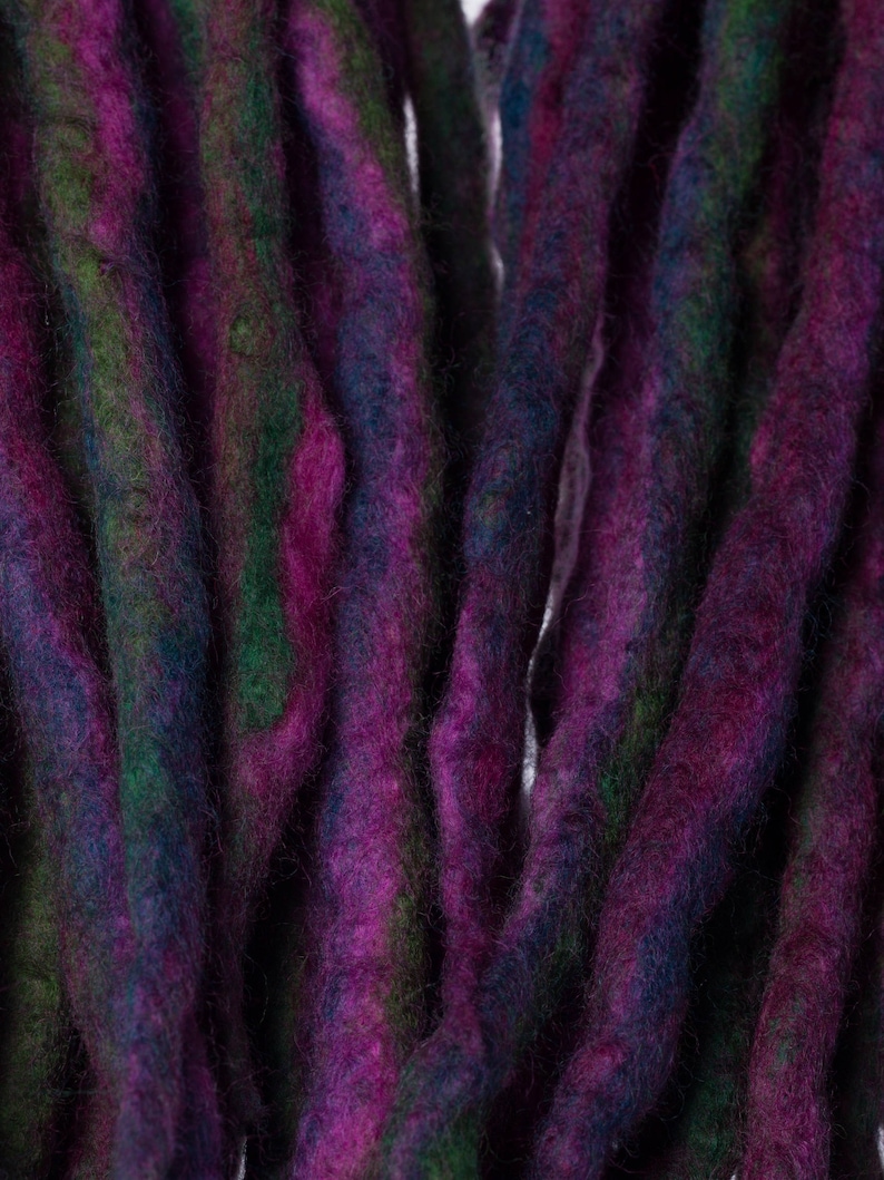 May include: Close-up of a bundle of purple, green, and blue wool dreadlocks.