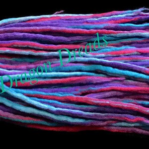 May include: A bundle of colorful wool dreadlocks in shades of blue, purple, and pink. The dreadlocks are long and straight, and they are arranged in a neat pile.
