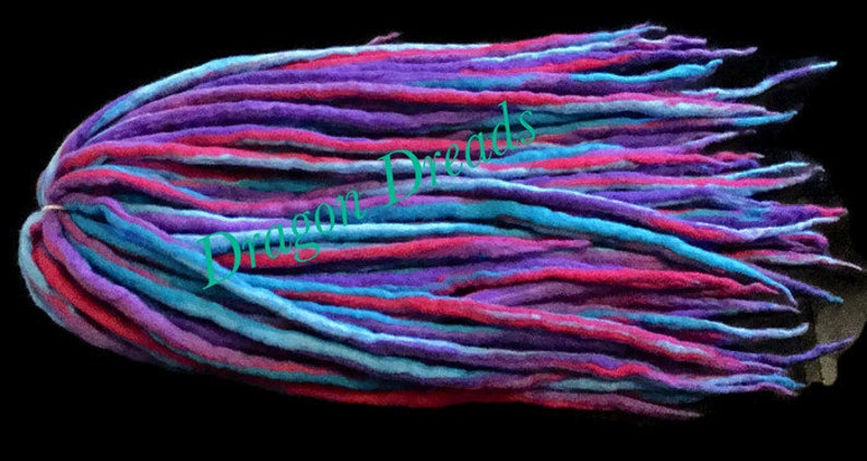 May include: A bundle of colorful wool dreadlocks in shades of blue, purple, and pink. The dreadlocks are long and straight, and they are arranged in a neat pile.