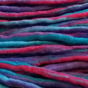 May include: A bundle of colorful wool yarn in shades of pink, blue, and purple. The yarn is arranged in a layered pattern, creating a textured and visually appealing display.