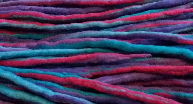 May include: A bundle of colorful wool yarn in shades of pink, blue, and purple. The yarn is arranged in a layered pattern, creating a textured and visually appealing display.