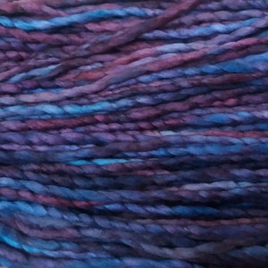 May include: A close-up of a skein of yarn with a deep purple and blue color gradient. The yarn is twisted and textured, creating a unique look.