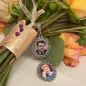 May include: A silver-toned metal pendant featuring two oval frames with ornate filigree borders. The top frame contains a black and white portrait of a man wearing glasses, while the bottom frame holds a color portrait of a woman.