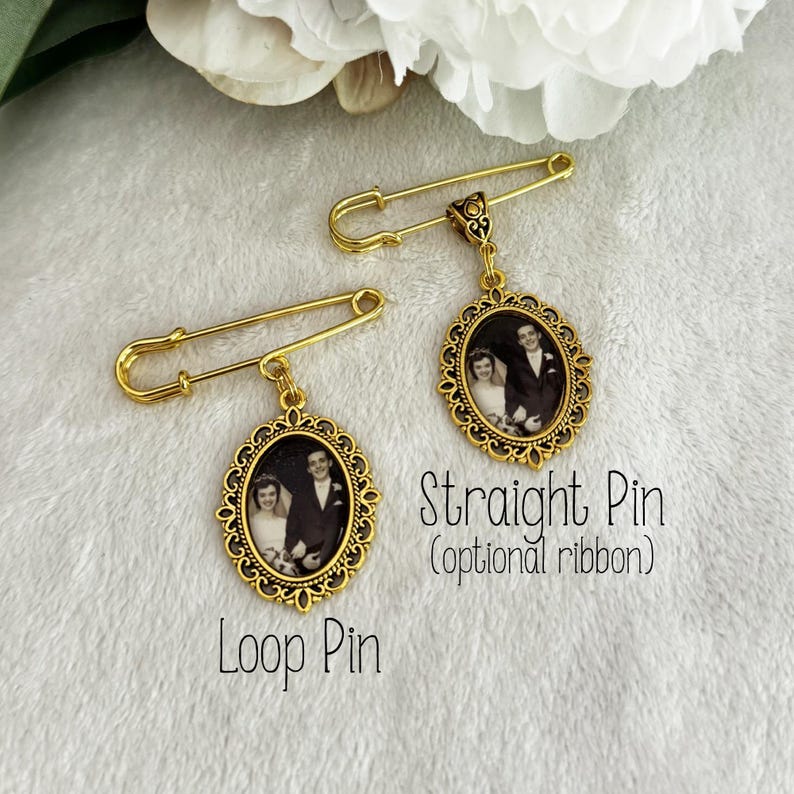 May include: Two gold-toned metal safety pins featuring oval-shaped pendants with ornate filigree borders. Each pendant contains a black and white photograph of a couple. The left pin has a loop attachment, and the right pin is a straight pin.