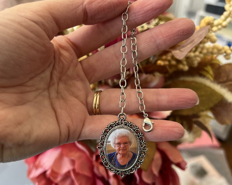 May include: Silver chain with a silver oval locket featuring a photo of an older woman with white hair. The locket has a decorative border.