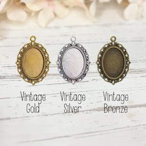 May include: Three oval pendant trays with ornate filigree borders in vintage gold, vintage silver, and vintage bronze finishes. Each metal frame features a small loop at the top for attachment. Text below reads: Vintage Gold, Vintage Silver, Vintage Bronze.