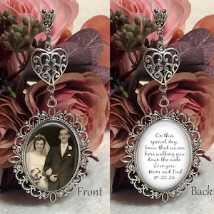May include: A silver heart-shaped charm hangs from a silver oval frame with a black and white photo of a bride and groom. The back of the frame has the text "On this special day, know that we are here walking you down the aisle. Love you. Mom and Dad 10.22.24".