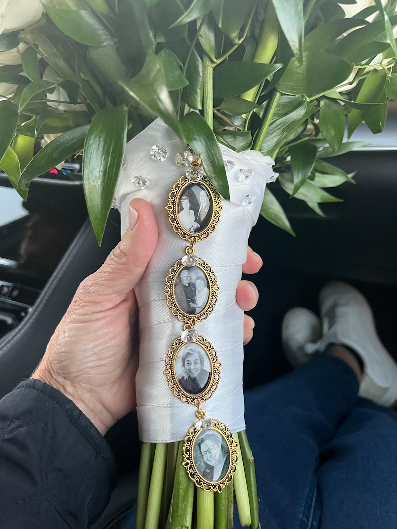 May include: A wedding bouquet wrapped in white satin ribbon with scattered clear crystals, featuring a vertical gold-toned metal charm strand with four oval frames containing black and white portrait photographs of individuals.