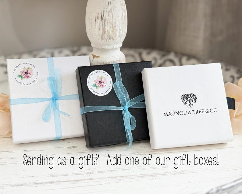 May include: Three gift boxes: white, black, and white. Each box is tied with a light blue ribbon. The white boxes have a floral sticker and the text "MAGNOLIA TREE & CO." The image includes the text "Sending as a gift? Add one of our gift boxes!"