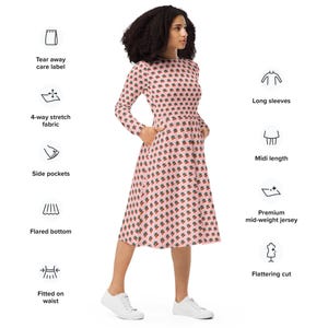 May include: A pink midi dress with a repeating pattern of green and red designs. The dress features long sleeves, side pockets, and a flared bottom. Made from a 4-way stretch fabric, it has a flattering cut and is fitted at the waist.