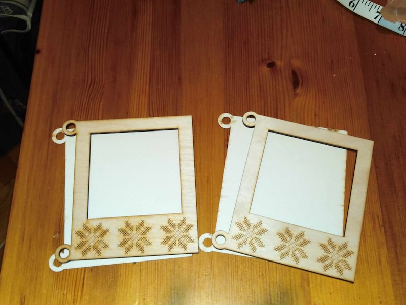May include: Two unfinished wooden picture frames with a white background and a snowflake design. The frames are approximately 6 inches by 6 inches.