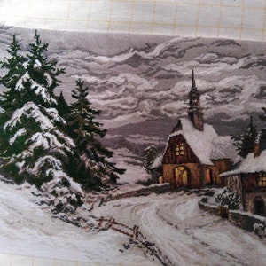 May include: A cross-stitch embroidery depicting a snowy winter scene with a small church, two pine trees, and a winding path leading to the church. The sky is a light gray with fluffy clouds.