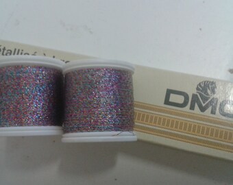 May include: Two spools of DMC metallic thread, one pink and one blue, with a silver shimmer. The spools are labeled "Fil métallique" and "DMC".