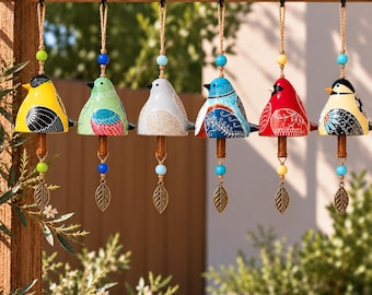 May include: Six ceramic bird-shaped wind chimes hanging in a row. Each bird features unique colourful patterns, including yellow, green, light blue, dark blue, red, and cream. Each chime includes a wooden clapper and a metal leaf charm.
