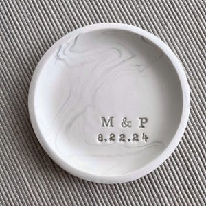 Peut inclure: Un plat à bagues en céramique blanche avec un motif marbré. Le plat est gravé des initiales "M & P" et de la date "8.22.24".