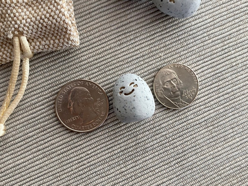 Thumb-sized rock shaped figurine with happy emoji expression in between a quarter and nickel for size comparison