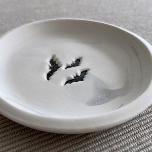 May include: A white ceramic trinket dish with a gray marbled design and a black tree silhouette in the center.