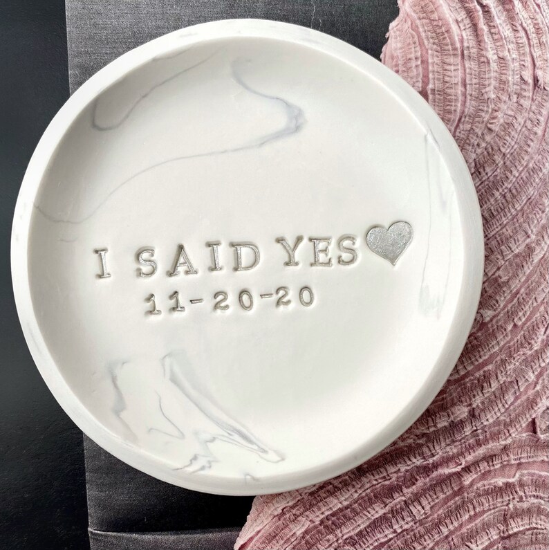 May include: White marble ring dish with the words "I said yes 11-20-20" and a small silver heart.