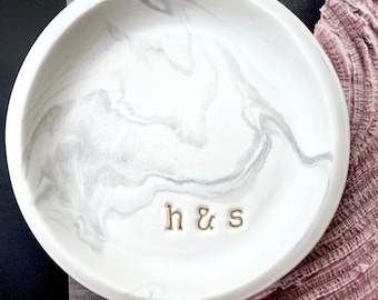 May include: White ceramic dish with a gray marble pattern and gold lettering that reads "h & s".