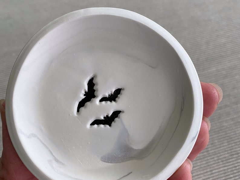 May include: White ceramic dish with a marbled design and three black bat silhouettes.