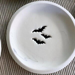 May include: White ceramic dish with a marbled design and three bat cutouts.