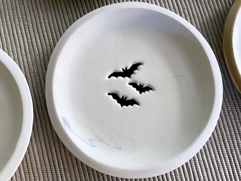 May include: White ceramic dish with a marbled design and three bat cutouts.