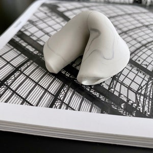 May include: A white ceramic fortune cookie with a gray marbled design. The cookie is sitting on a black and white photo of a building.