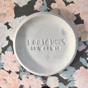 May include: White ceramic ring dish with a marbled design. The dish is engraved with the text "i said yes" and the date "12 20 18".