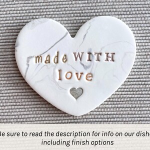 May include: White ceramic heart-shaped dish with a marbled pattern. The dish has the words "made WITH love" inscribed on it in gold lettering.