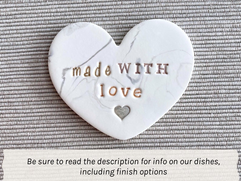 May include: White ceramic heart-shaped dish with a marbled pattern. The dish has the words "made WITH love" inscribed on it in gold lettering.