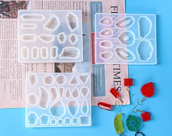 May include: Three clear silicone molds for making resin jewelry. The molds are shaped like different types of rocks and crystals. There are several finished resin earrings in the image, including red, green, and clear.