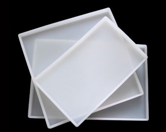 May include: Three white silicone trays of different sizes, stacked on top of each other. The trays are rectangular and have a smooth surface.