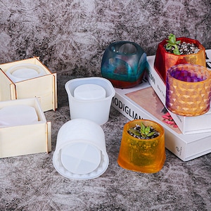 May include: Assortment of silicone molds for making resin planters. The molds are in various shapes, including round, square, and geometric. There are also finished resin planters in different colors, including orange, purple, and teal.