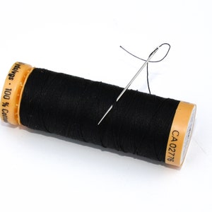 May include: A black cotton thread spool with a needle threaded through it. The spool has yellow and orange labels. The thread is 100% cotton. The needle is silver and the thread is black.