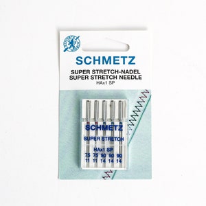 May include: A pack of five Schmetz Super Stretch sewing machine needles, model HAx1 SP, in a clear plastic case on a white card. The needles are labelled with sizes 75/11 and 90/14, featuring blue and red colour-coded bands on the needle shanks.
