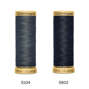 Könnte beinhalten: Zwei Spulen Gütermann Nähgarn in Dunkelgrau und Marineblau. Jede Spule ist mit dem Gütermann-Logo und Produktinformationen versehen, einschließlich 100 m. Die Produktcodes 5104 und 5902 sind sichtbar.