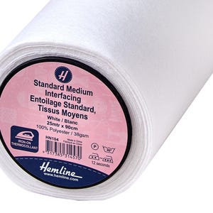 Könnte beinhalten: Eine Rolle weißen Standard-Mittelvliesstoffs. Das Etikett lautet "Standard Medium Interfacing, Weiß, 25 m x 90 cm, 100 % Polyester". Das Etikett enthält auch den Text "Iron-on Thermocollant".