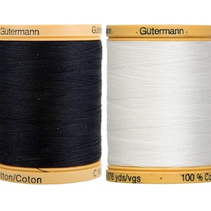 May include: Two Gütermann thread spools, one black and one white, are shown. The spools have beige tops and bases, with the brand name printed on them. The white spool has "876 yds/vgs" and "100% Cotton" printed on it. The thread is 100% cotton.