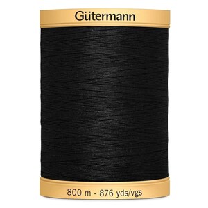 May include: A spool of black G&uuml;termann sewing thread with a tan top and bottom label. The top label displays the brand name G&uuml;termann, and the bottom label indicates a length of 800 m - 876 yds/vgs. The thread is wound tightly around the spool.