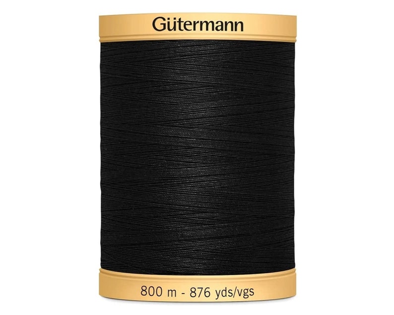 May include: A spool of black G&uuml;termann sewing thread with a tan top and bottom label. The top label displays the brand name G&uuml;termann, and the bottom label indicates a length of 800 m - 876 yds/vgs. The thread is wound tightly around the spool.