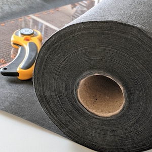 May include: A roll of black fabric, probably felt, is shown on a table. The fabric is rolled up tightly and the end of the roll is visible. A yellow and black rotary cutter is also shown in the image.