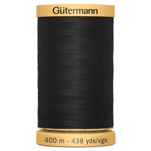 May include: A spool of black sewing thread with a tan top and bottom. The top label reads G&uuml;termann in black text. The bottom label displays the length as 400 m - 438 yds/vgs. The thread is wound tightly around the cylindrical spool body.
