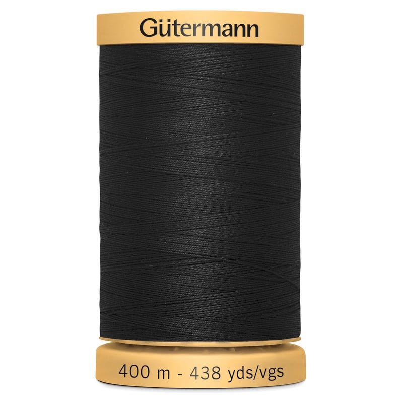 May include: A spool of black sewing thread with a tan top and bottom. The top label reads G&uuml;termann in black text. The bottom label displays the length as 400 m - 438 yds/vgs. The thread is wound tightly around the cylindrical spool body.