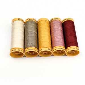May include: Five spools of Gutermann thread in various colors: off-white, gray, mustard yellow, mauve, and burgundy. Each spool has a yellow base and a label with the brand name and thread length.