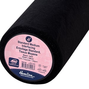 Könnte beinhalten: Eine Rolle schwarzes Standard-Mittelvlies. Das Etikett lautet "Standard Medium Interfacing, Entoilage Standard, Tissus Moyens". Die Rolle ist 25 Meter lang und 90 cm breit, aus 100 % Polyester.